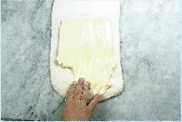 Picture of softened butter being spread over surface of dough